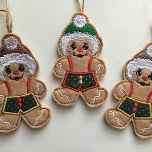 May include: Three gingerbread man ornaments with white fur hats, green and red accents, and brown bodies. The ornaments are hanging from twine.