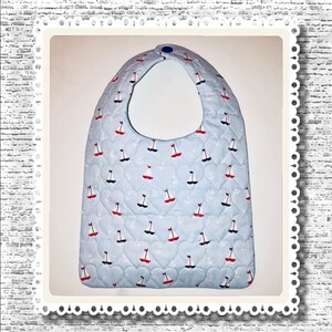 May include: A light blue baby bib with a white quilted pattern of small hearts and sailboats. The bib has a blue button at the top.