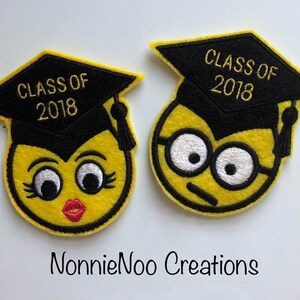 May include: Two yellow felt embroidered patches with a graduation cap and the text "Class of 2018". One patch has a female face with eyelashes and lipstick. The other patch has a male face with glasses.
