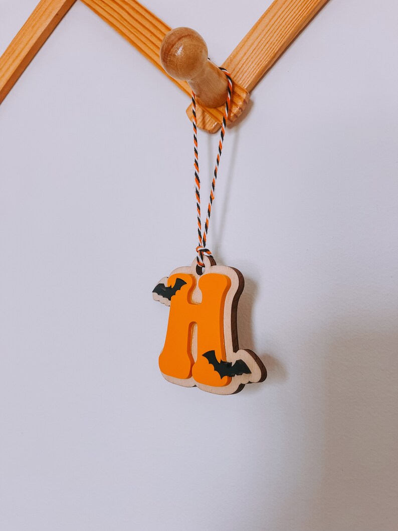 May include: Orange wooden letter H with black bats hanging from a string. The letter is hanging from a wooden hook.