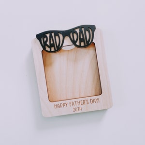 K&ouml;nnte beinhalten: Ein Holzbildrahmen mit einem Ausschnitt von einer Sonnenbrille, auf dem oben "Rad Dad" steht. Der Rahmen hat den Text "Happy Father's Day! 2024" unten eingraviert.