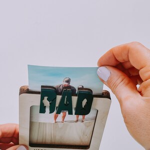 Może przedstawiać: Drewniana ramka na zdjęcia z napisem "DAD" w zielonych literach i sylwetką ryby. Ramka ma miejsce na zdjęcie i napis "Happy Father's Day!" z sylwetką ryby.