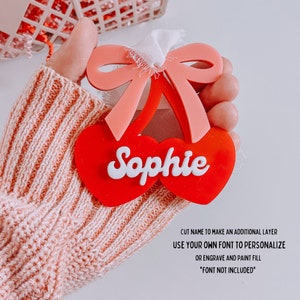 May include: Red and pink cherry-shaped ornament with a white bow and the name "Sophie" written in white. The ornament is made of acrylic and can be personalized with a custom font.