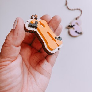 May include: Two Halloween-themed wooden ornaments, one shaped like the letter "B" and the other like the number "3". The "B" is orange with black bats and white trim. The "3" is purple with black bats and white trim.