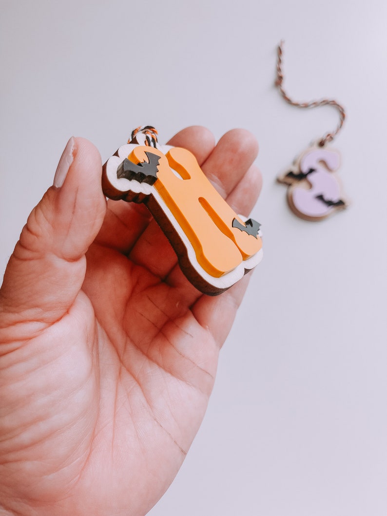 May include: Two Halloween-themed wooden ornaments, one shaped like the letter "B" and the other like the number "3". The "B" is orange with black bats and white trim. The "3" is purple with black bats and white trim.