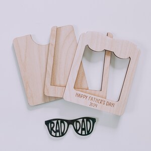 K&ouml;nnte beinhalten: Holzrahmen mit dem Text "Happy Father's Day! 2024" und einer schwarzen Sonnenbrille mit dem Text "Rad Dad" auf den Gl&auml;sern.