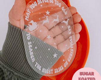 May include: A white oval ornament with the text "May you never be too old to search the night skies on Christmas Eve" and a silhouette of Santa Claus in a sleigh pulled by reindeer. The ornament is laser ready and is an SVG file.