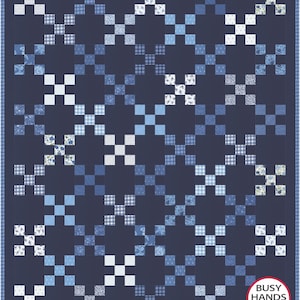 Op de afbeelding: Een rechthoekige quilt met een herhalend X-patroon bestaande uit diverse blauwe en witte stoffen vierkanten. Het ontwerp bevat effen marineblauwe blokken afgewisseld met lichtblauwe, witte en bedrukte vierkanten. Een logo vermeldt BUSY HANDS QUILTS.