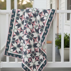 May include: A quilt featuring a repeating star pattern in dark teal, white, and soft pink floral fabric. The design includes a wide border with a dark teal floral print and a thin pink binding. The text Busy Hands Quilts is in the corner.