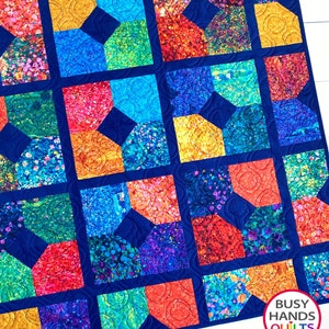 May include: A colorful quilt with a geometric pattern of squares and diamonds. The quilt is made with a variety of fabrics in shades of blue, green, red, orange, and yellow. The quilt is quilted with a swirling pattern. The quilt is labeled "Busy Hands Quilts" in the bottom right corner.