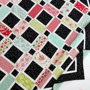 May include: A colorful quilt with a geometric design. The quilt features a pattern of black squares and rectangles, with alternating sections of patterned fabric in shades of red, pink, green, and teal. The quilt is handmade.