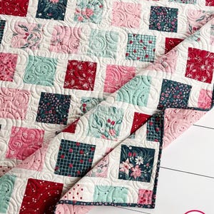 May include: A quilt made of various floral patterned fabrics in shades of pink, red, green, and blue. The quilt is quilted with a swirl pattern and has a pink binding.