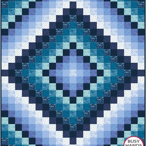 May include: A quilt pattern featuring a diamond shape in the centre. The quilt is made from blue and white fabric with a gradient effect. The fabric has a small floral pattern. The quilt is surrounded by a border of white fabric.