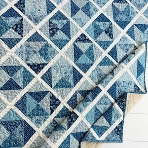 Puede incluir: Un edredón hecho a mano con un diseño geométrico en tonos azules y blancos. El edredón presenta un patrón de rejilla de diamantes creado a partir de cuadrados y triángulos. Los bordes están acabados con un borde blanco y un reverso color crema.