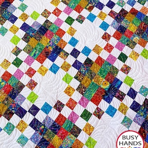 May include: A colourful quilt with a white background and a geometric pattern. The quilt is made of squares of different colours and patterns, including red, blue, green, yellow, and purple. The quilt is quilted with a swirl pattern. The quilt is labelled "Busy Hands Quilts" in the bottom right corner.