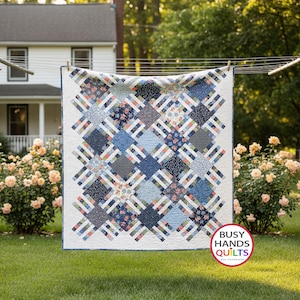 May include: A square quilt featuring a repeating pattern of blue, white, and coral floral and geometric fabric squares connected by white lattice strips. The quilt has a white border and a logo in the corner that reads BUSY HANDS QUILTS.
