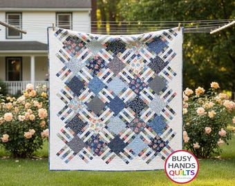May include: A square quilt featuring a repeating pattern of blue, white, and coral floral and geometric fabric squares connected by white lattice strips. The quilt has a white border and a logo in the corner that reads BUSY HANDS QUILTS.