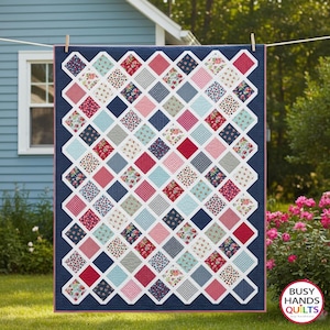 May include: A rectangular quilt featuring a grid of diamond-shaped fabric patches in various floral, polka dot, and gingham patterns in shades of red, pink, blue, and white, all set against a solid navy blue background with a thin red border.