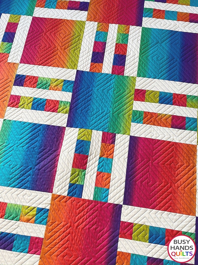 May include: A colorful quilt with a geometric pattern. The quilt is made up of squares of different colors, including red, orange, yellow, green, blue, and purple. The squares are arranged in a grid pattern, and the quilt is quilted with a simple straight stitch. The quilt is signed "Busy Hands Quilts" in the bottom right corner.