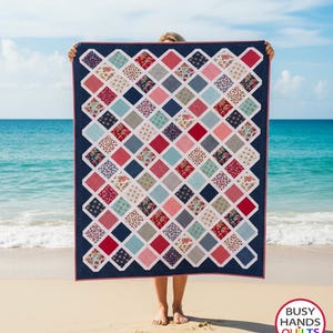 May include: A rectangular quilt featuring a diamond-patterned grid of multi-colored fabric squares in shades of red, blue, pink, and white, bordered by a dark navy blue frame. The quilt displays the text BUSY HANDS QUILTS buy handmade in a circle.