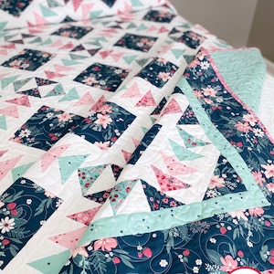 May include: A quilt with a navy blue background and a pattern of pink and green triangles. The quilt is edged with a light blue and pink border. The quilt is made by Busy Hands Quilts, buy handmade.