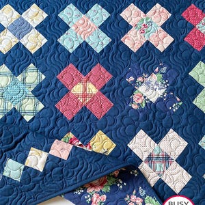 Puede incluir: Una colcha de retazos acolchada azul con una variedad de patrones florales y geométricos. La colcha está doblada por la mitad y el borde inferior es visible. La colcha está hecha por Busy Hands Quilts, una empresa que hace colchas hechas a mano.