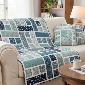Pode incluir: Uma colcha retangular e uma almofada quadrada a condizer com um design de patchwork de vários tecidos azuis, verde-azulados e brancos com padrões florais e de animais da floresta, separados por faixas brancas finas e um rebordo branco.