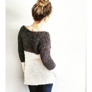 Puede incluir: Un suéter de punto grueso con un diseño de bloques de color blanco y negro. El suéter tiene un corte holgado y una silueta ligeramente oversized.