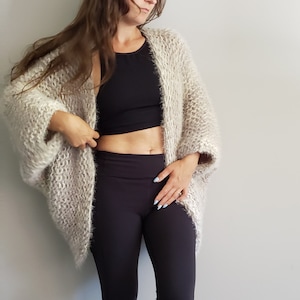 May include: A light brown fuzzy knit cardigan with a long, open front and long sleeves. The cardigan is worn over a black tank top and black leggings.