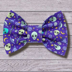 May include: Purple bow tie with a space alien and spaceship pattern. The bow tie has a green, blue, and white colour scheme.