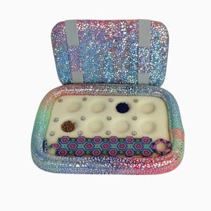 May include: A rectangular storage case with a holographic cracked-glass pattern containing a foam insert with twelve labelled circular indentations. Inside are two small piles of beads and a woven beaded bracelet with a geometric pattern.