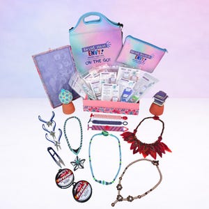 May include: A collection of jewelry-making supplies, including pliers, wire, beads, and necklaces. The image also features a pink box with packets, a tie-dye lunch bag, and a matching pouch, all branded with "bead mat ENVY! ON THE GO!"