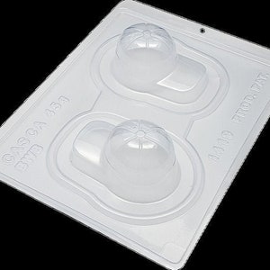 Op de afbeelding: Witte plastic mal met twee holtes in de vorm van baseballpetten. De mal is gelabeld "CASCA 439 BWB" en "14119 PROD. PAT."