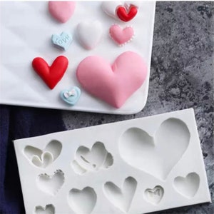Może przedstawiać: Biała silikonowa forma z dziewięcioma wnękami w kształcie serca. Forma jest przeznaczona do robienia czekolady, fondantu lub innych jadalnych dekoracji.