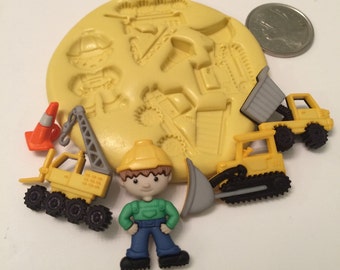 Puede incluir: Un molde de silicona amarillo con un diseño de trabajador de la construcción. El molde está rodeado de pequeños juguetes de construcción de plástico, incluyendo un trabajador de la construcción, una grue, un camión de volteo, una excavadora y un cono de tráfico.