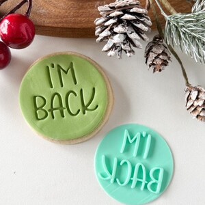 May include: Two green and blue cookie cutters with the text "I'm Back" in white lettering. The cookie cutters are on a white surface.