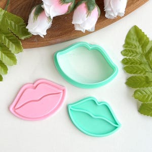 Peut inclure: Deux emportes-pièces en plastique en forme de lèvres. L'un est rose et l'autre est vert.