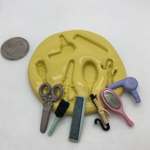 May include: A silicone mold for making miniature hair styling tools. The mold includes a hair dryer, comb, scissors, hair brush, and a curling iron. The mold is yellow and the tools are in various colors.