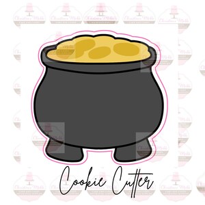 Puede incluir: Cortador de galletas de caldero negro con una sustancia amarilla, similar al oro, en su interior. El cortador tiene tres patas cortas. El texto "Cookie Cutter" está escrito debajo de la imagen.