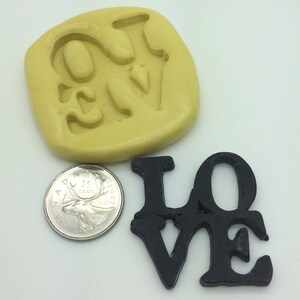 May include: A silicone mold for making a LOVE sign. The mold is yellow and the sign is black. The sign is about the size of a Canadian quarter.