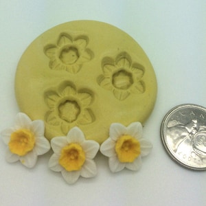 May include: A yellow daffodil flower mould with three flower impressions, next to three finished white and yellow daffodils. A coin is included for size reference. The daffodils have white petals and yellow centres.