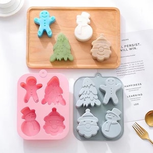 Op de afbeelding: Twee siliconen mallen voor het maken van kerstthema zeep of snoep. De roze mal heeft vier holtes: een peperkoekman, een kerstboom, een sneeuwpop en de kerstman. De grijze mal heeft vier holtes: een kerstboom, een peperkoekman, een sneeuwpop en de kerstman.