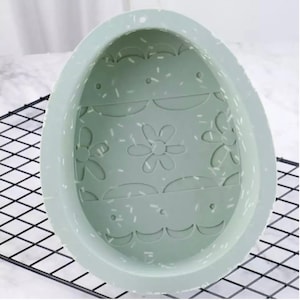 May include: A light green silicone Easter egg mold with a daisy pattern and sprinkles design. The mold is designed to create a hollow egg shape.