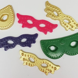 Pode incluir: Cinco máscaras de carnaval de diferentes cores e designs. As máscaras são feitas de plástico e têm um acabamento brilhante. As cores são dourado, rosa, roxo, verde e dourado.