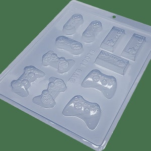 May include: A clear plastic mold for making chocolate game controllers and consoles. The mold has 9 cavities, including 7 different game controllers and 2 consoles. The mold is labeled "BWB 10028".