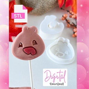 May include: A pink, cartoon-style cookie on a stick, with a red mouth and eye details. Beside it are two white plastic cookie cutters in the same shape. The image also includes a digital download file icon.
