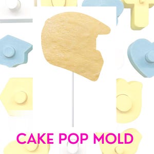 Puede incluir: Un molde amarillo para cake pops con forma de casco. El molde está hecho de plástico y tiene una superficie lisa. El molde está rodeado de otros moldes para cake pops de varias formas y colores.