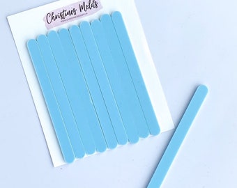 May include: A set of ten light blue popsicle sticks, with one stick lying separately. The sticks are approximately 7.5 cm long. The sticks are on a white background with the text "Christine's Molds" printed on the background.