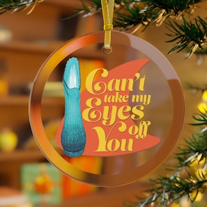 May include: A clear, round Christmas ornament with a gold ribbon. The ornament features a teal vase graphic and the text "Can't take my Eyes off You" in orange and yellow.