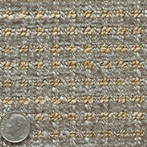 May include: Close-up of a textured fabric with a woven pattern in shades of beige, tan, and grey. A U.S. dime is in the lower left corner for scale, showing the fabric's fine detail and texture. The fabric appears to be a natural fibre.